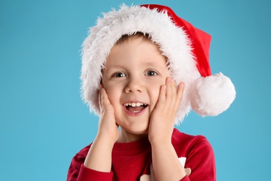 Cute child in Santa hat on light blue background. Christmas celebration