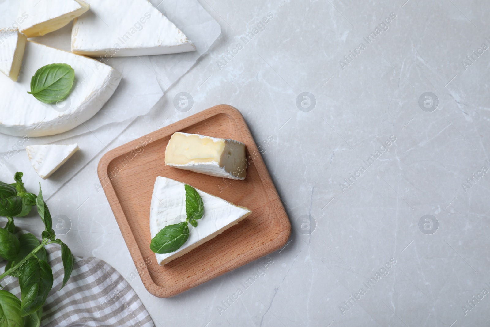 Photo of Delicious brie cheese with basil on light grey table, flat lay. Space for text