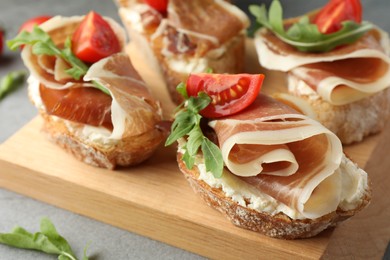 Photo of Tasty sandwiches with cured ham, tomatoes and arugula on wooden board, closeup