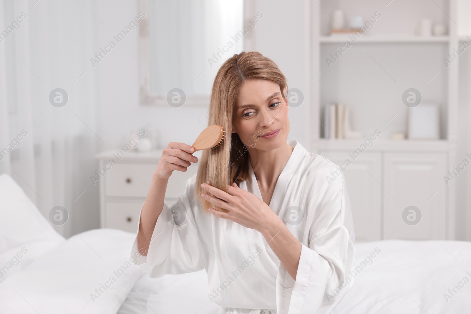 Photo of Beautiful woman brushing her hair on bed in room