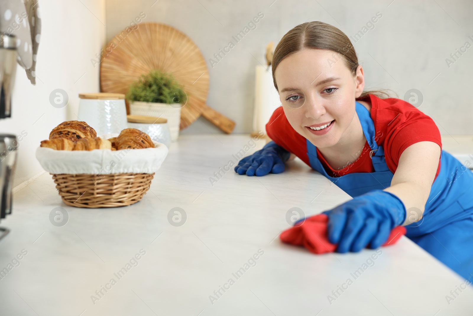 Photo of Woman cleaning white countertop with rag in kitchen