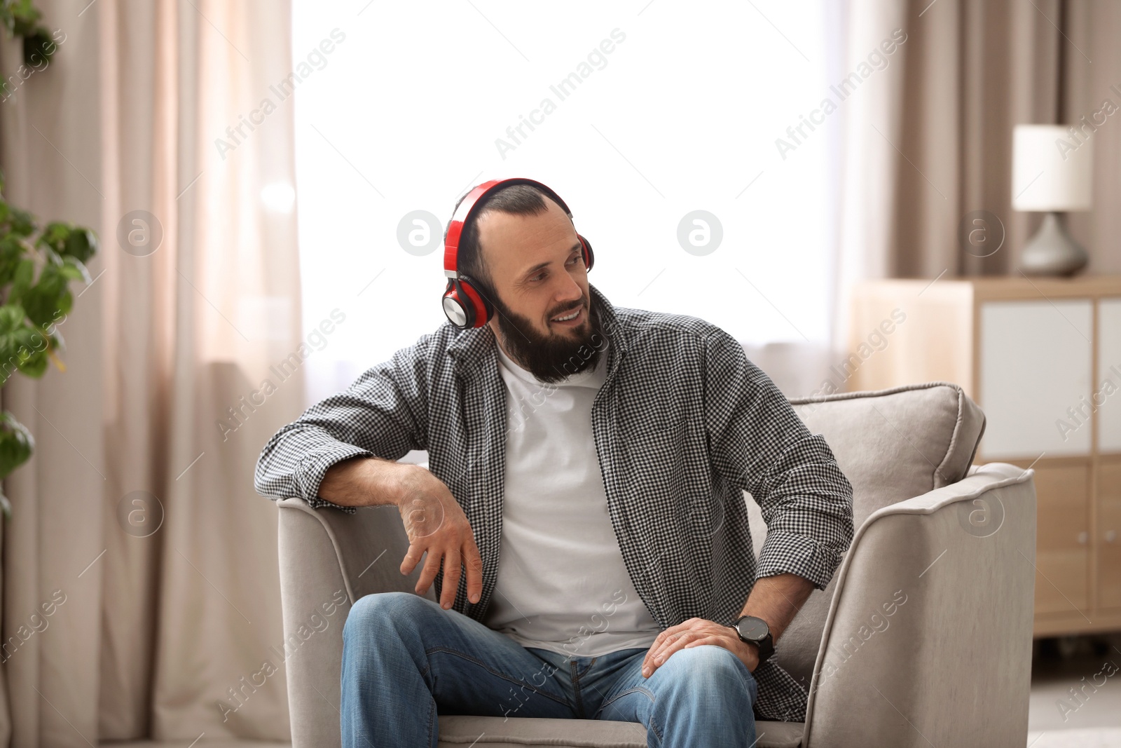 Photo of Mature man with headphones resting in armchair at home