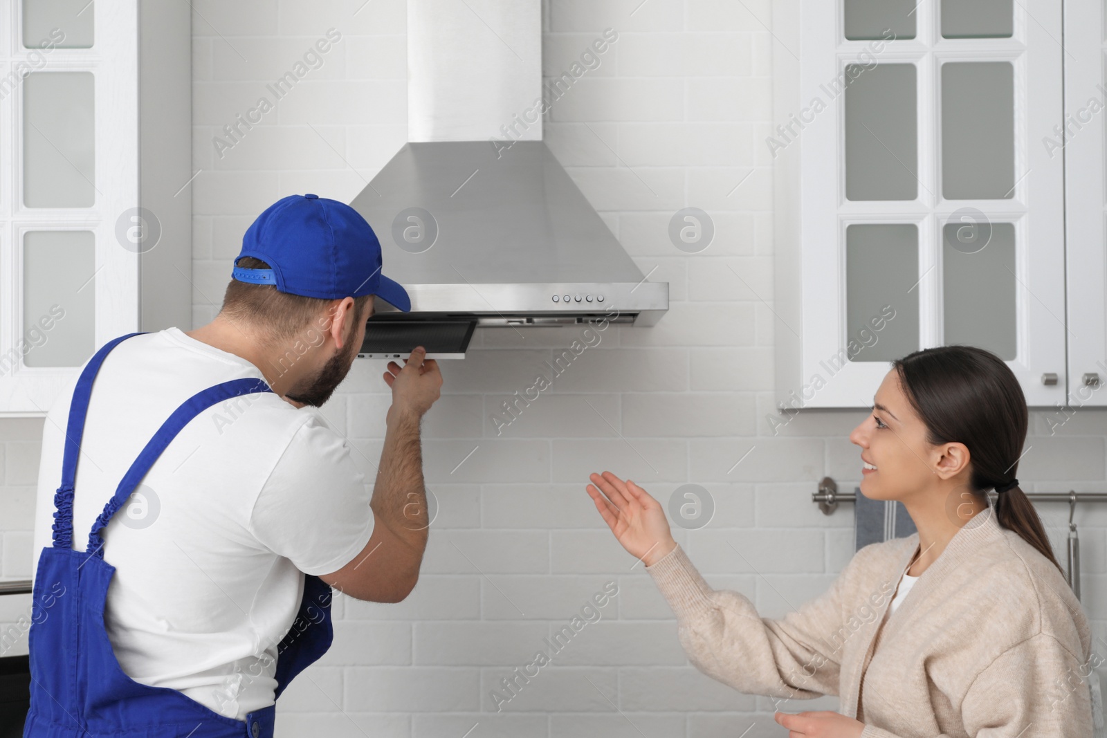 Photo of Worker repairing modern cooker hood and woman in kitchen