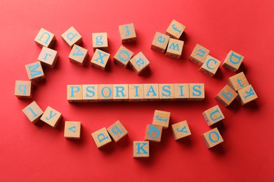 Word Psoriasis made of wooden cubes with letters on red background, flat lay