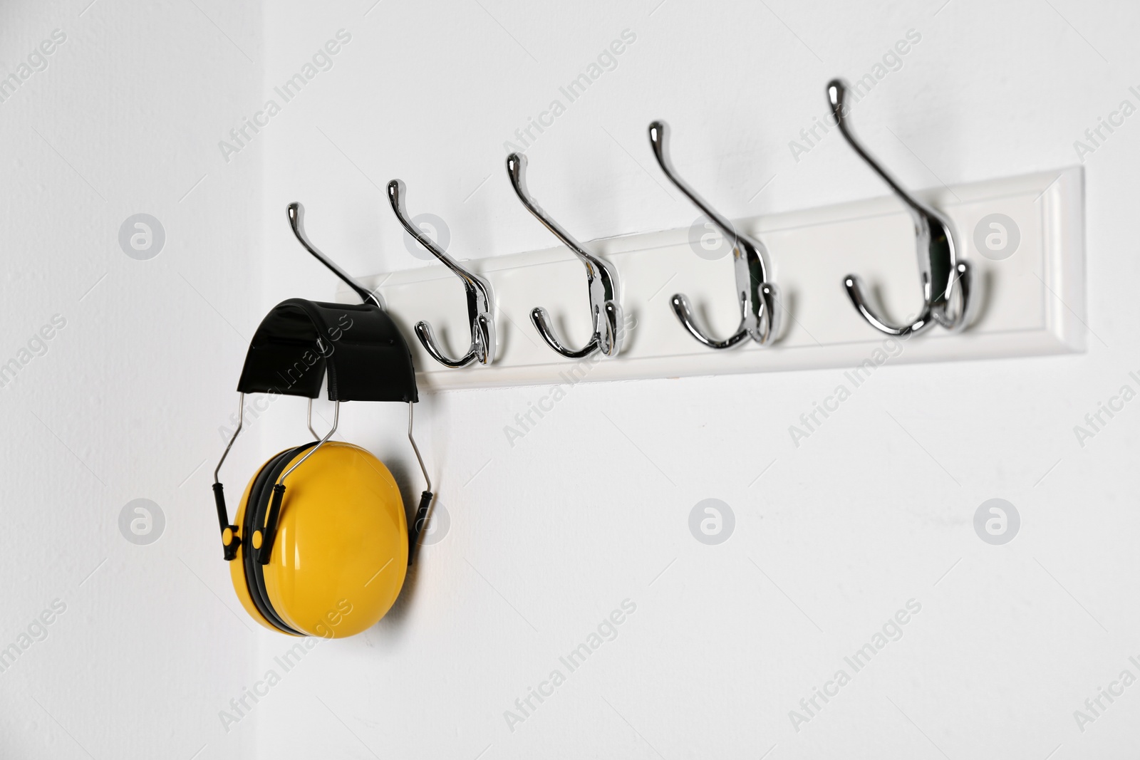 Photo of Protective headphones hanging on white wall. Safety equipment