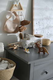 Wooden toys and different accessories on grey chest of drawers in child room