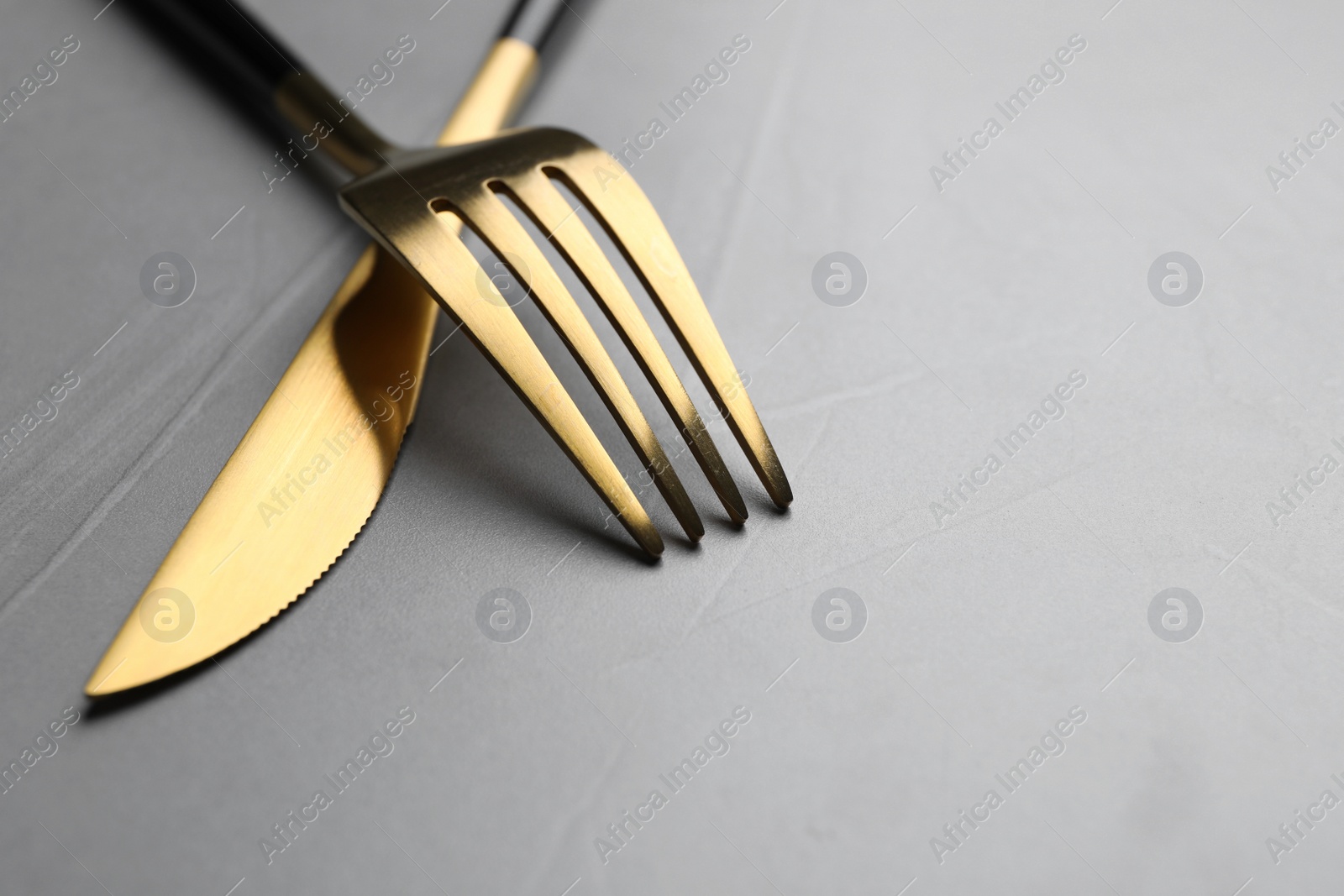 Photo of Golden fork and knife on grey table, closeup. Space for text