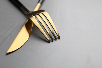 Photo of Golden fork and knife on grey table, closeup. Space for text
