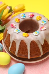 Delicious Easter cake decorated with sprinkles near beautiful tulips and painted eggs on yellow background