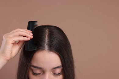 Woman with comb examining her hair and scalp on beige background, closeup. Space for text