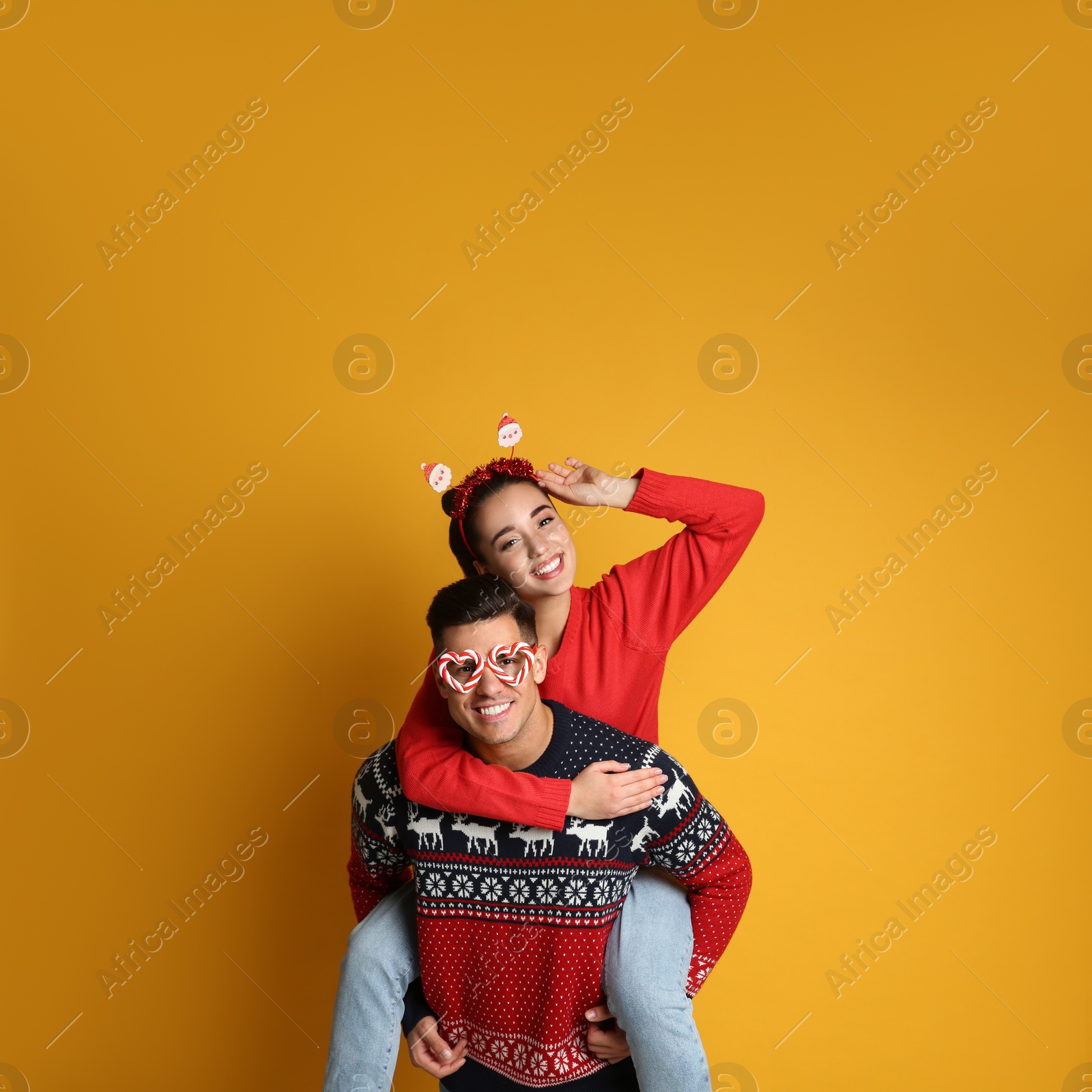 Photo of Couple in Christmas sweaters, Santa headband and party glasses on yellow background