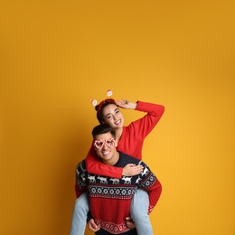Photo of Couple in Christmas sweaters, Santa headband and party glasses on yellow background