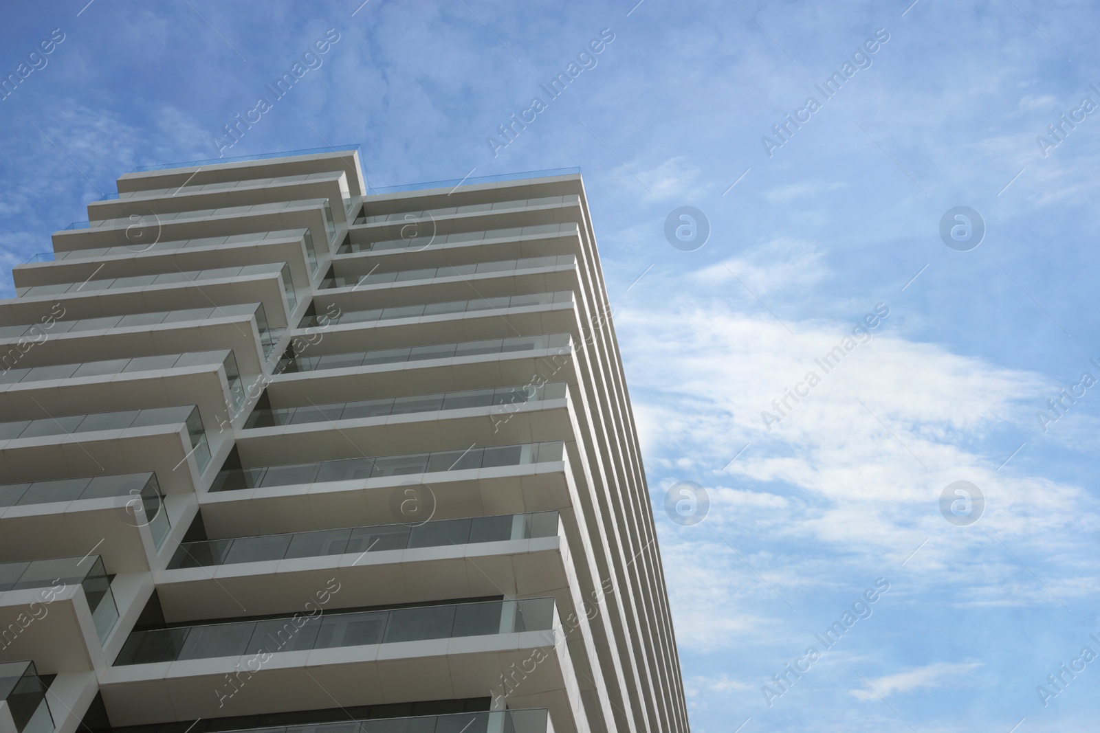 Photo of Exterior of residential building with balconies against blue sky, low angle view. Space for text