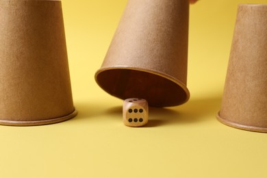 Three paper cups and dice on yellow background, closeup. Thimblerig game