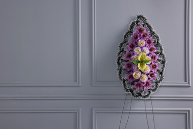 Photo of Funeral wreath of plastic flowers near light grey wall, space for text