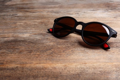 Photo of Stylish sunglasses on wooden background, space for text. Fashionable accessory