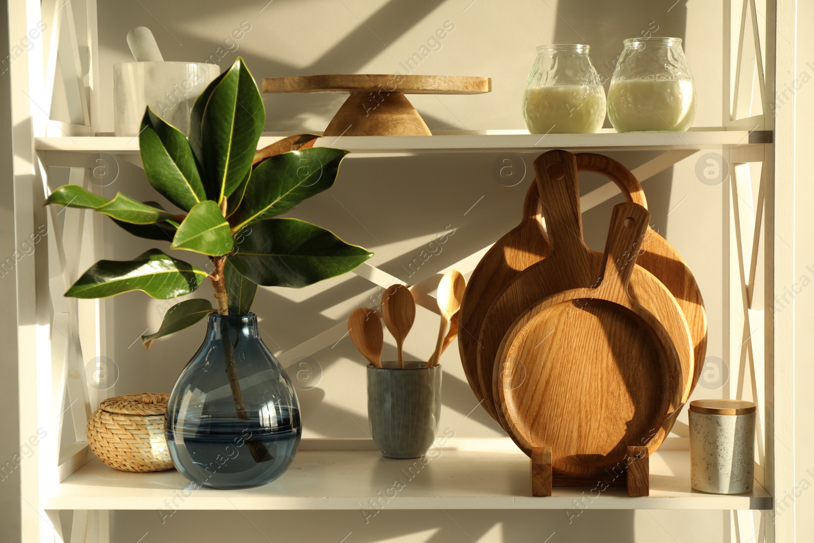 Photo of Wooden cutting boards, utensils, branch with green leaves and decor on shelving unit