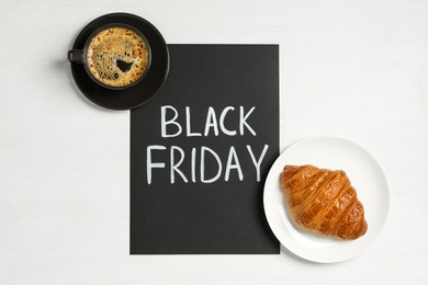 Photo of Cup of coffee, croissant and sheet of paper with words Black Friday on white background, flat lay