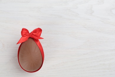 Photo of Sweet chocolate egg with red bow on white wooden table, top view. Space for text