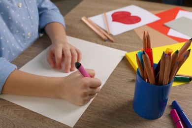 Photo of Little girl making beautiful greeting card at table indoors, closeup