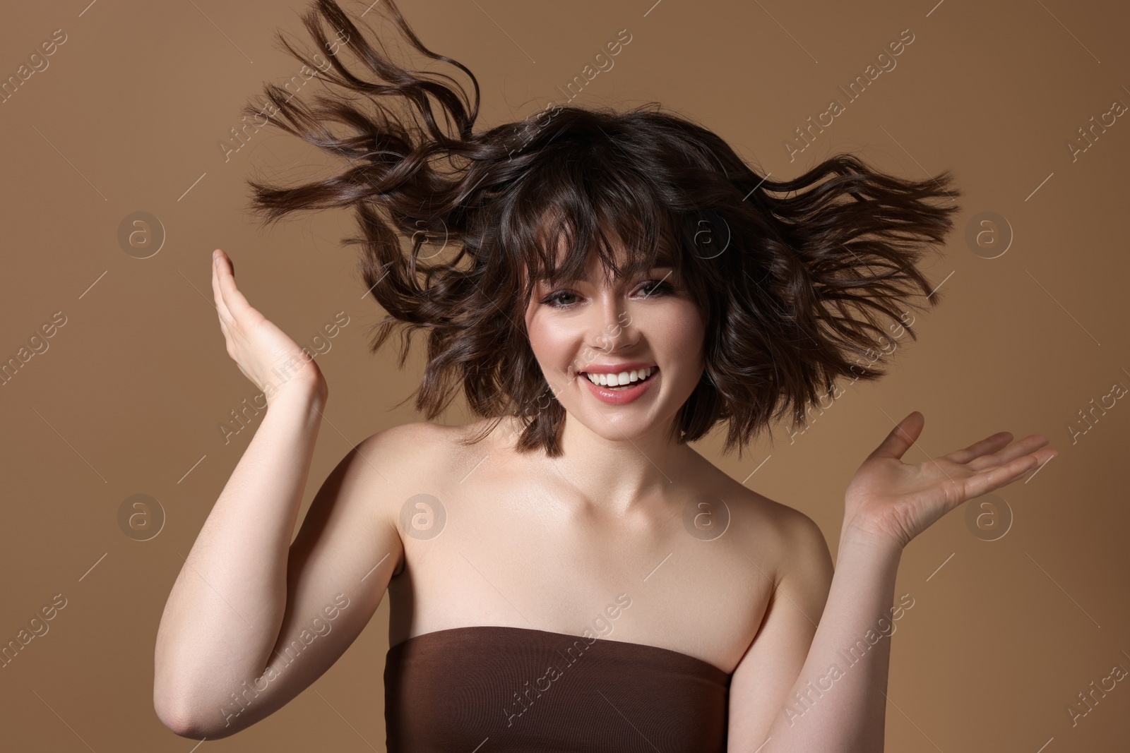 Photo of Portrait of beautiful young woman with wavy hairstyle on brown background