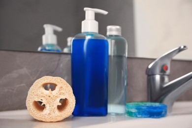 Photo of Loofah sponge and cosmetic products on sink in bathroom