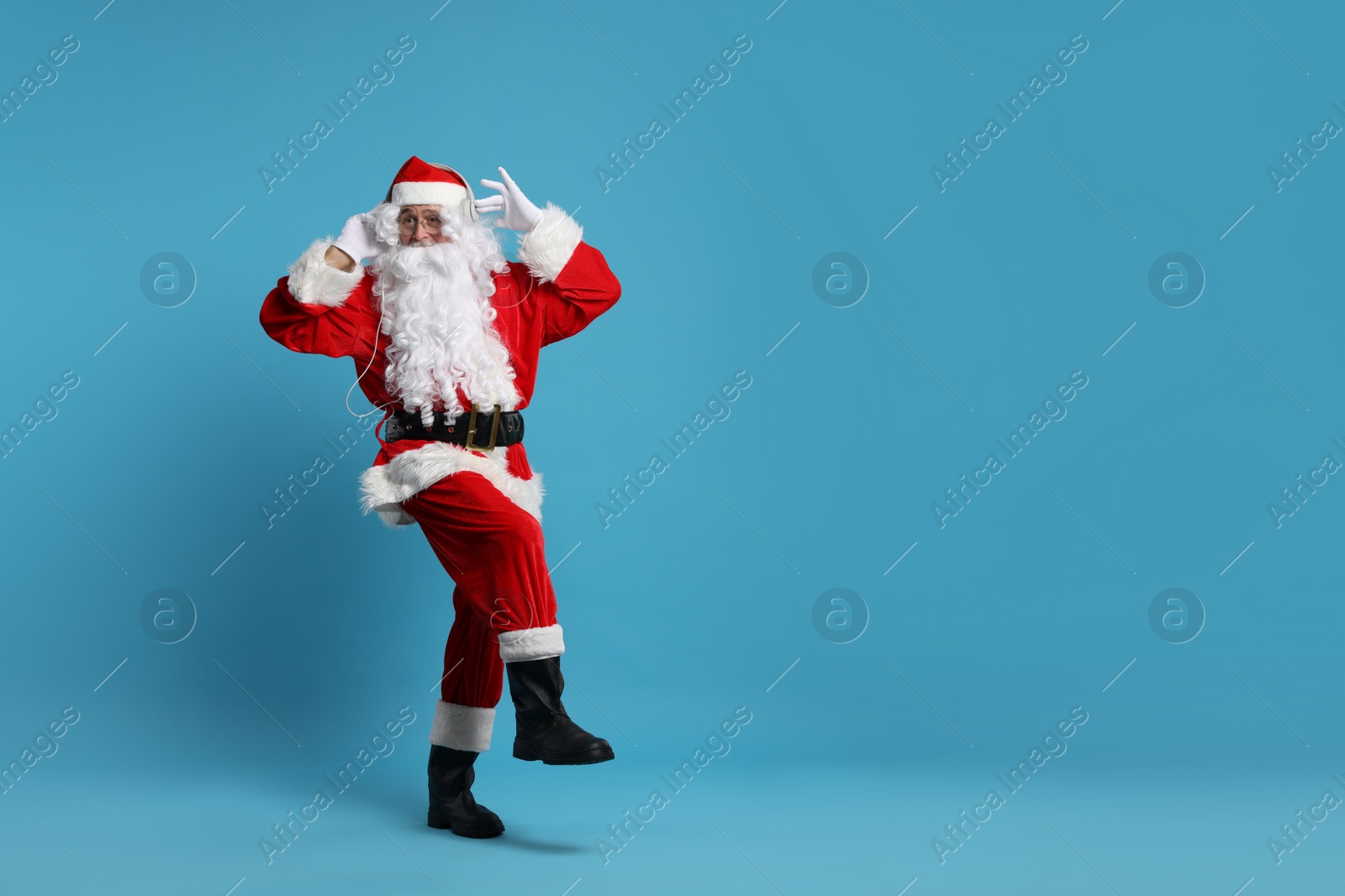 Photo of Merry Christmas. Santa Claus in headphones listening to music on light blue background, space for text