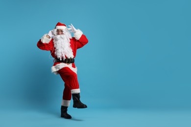 Merry Christmas. Santa Claus in headphones listening to music on light blue background, space for text