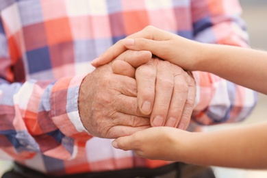 Photo of Young woman holding elderly man hands, closeup. Help service