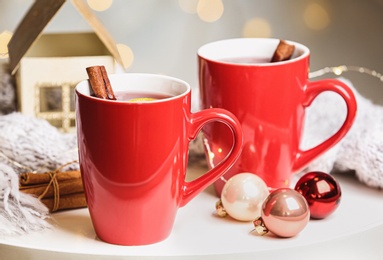 Photo of Cups of hot winter drink and Christmas decoration on table against blurred background