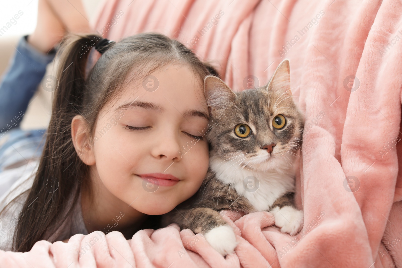 Photo of Cute little girl with cat lying on sofa at home