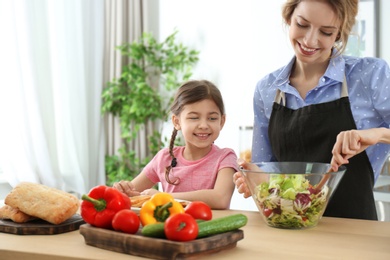 Young nanny with cute little girl cooking together in kitchen