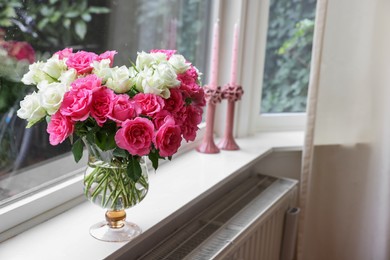 Photo of Vase with beautiful bouquet of roses and candles on windowsill indoors, space for text