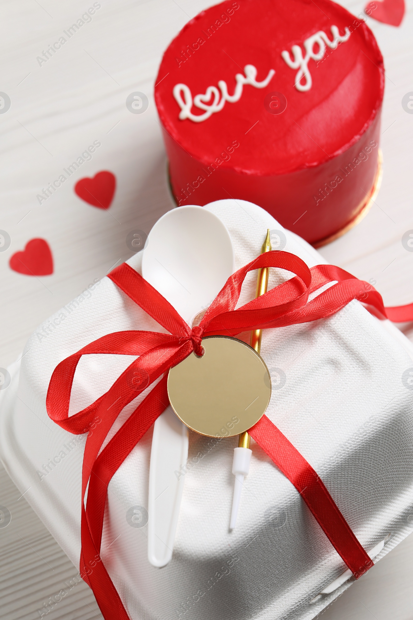 Photo of Bento cake with text Love You, takeaway packaging and paper hearts on white wooden table. St. Valentine's day surprise