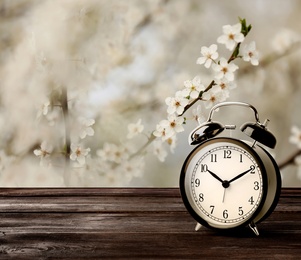 Image of Black alarm clock on wooden table, space for text. Daylight saving time (Spring forward)