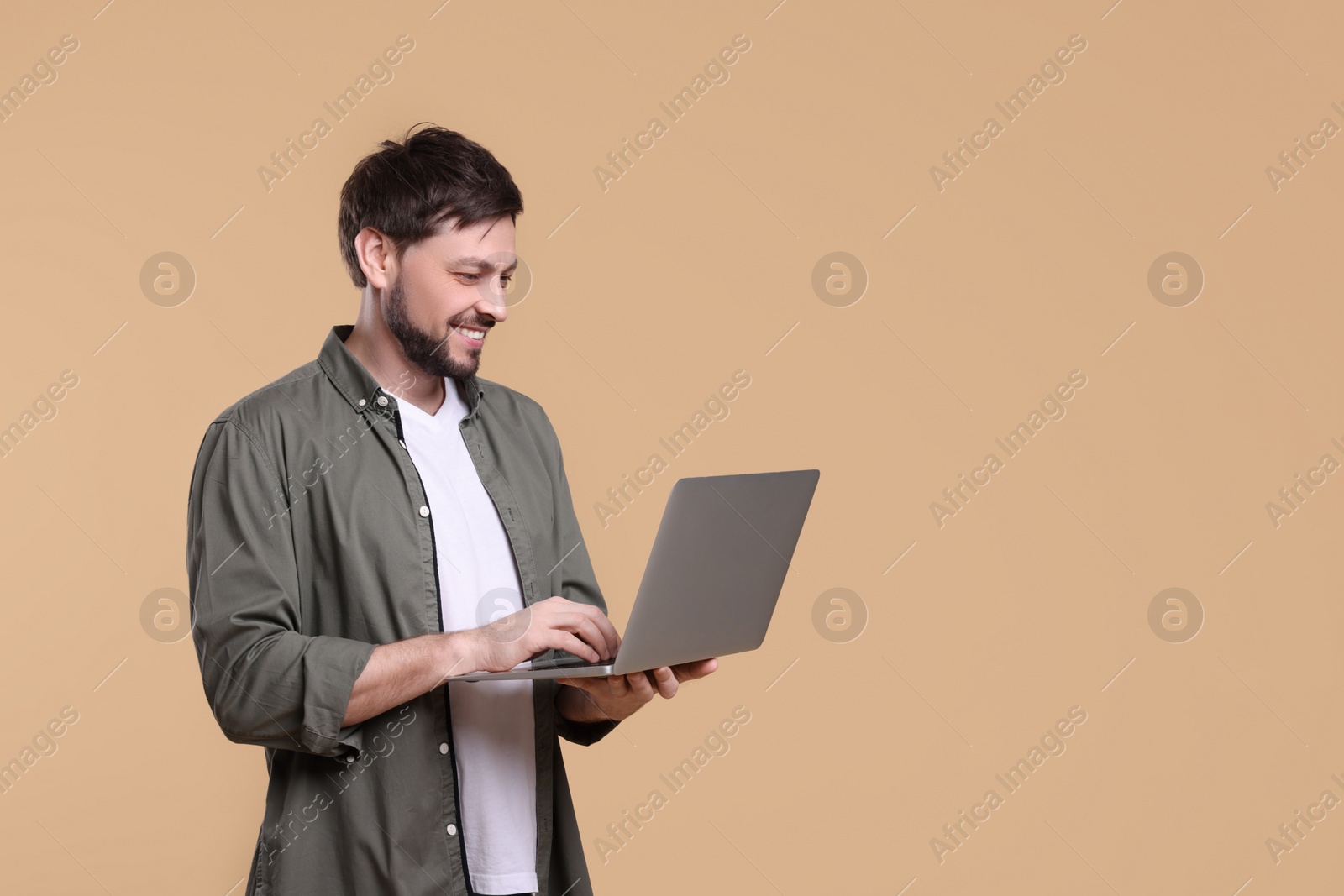 Photo of Happy man with laptop on beige background, space for text