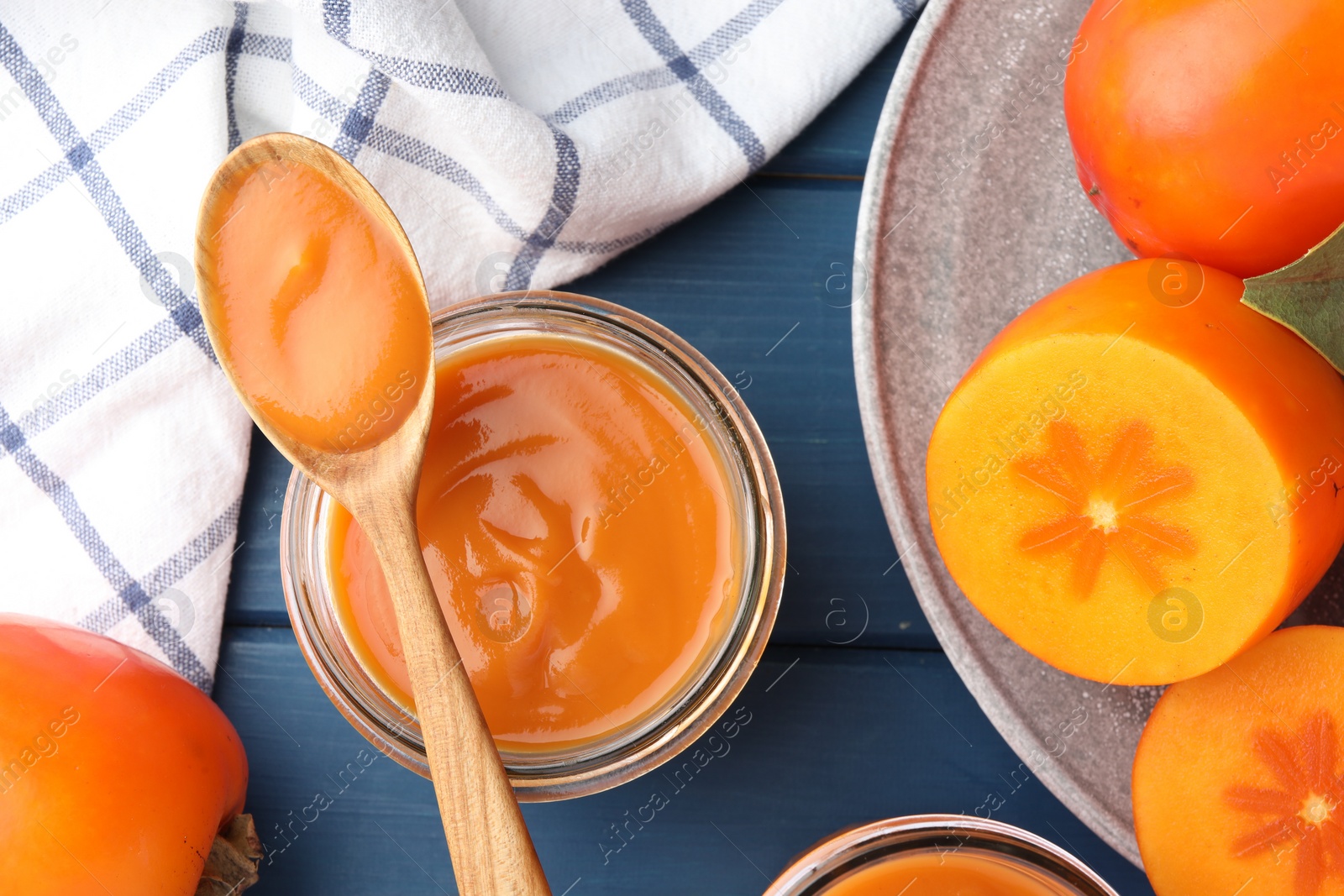 Photo of Delicious persimmon jam in glass jar served on blue wooden table, flat lay