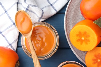 Photo of Delicious persimmon jam in glass jar served on blue wooden table, flat lay