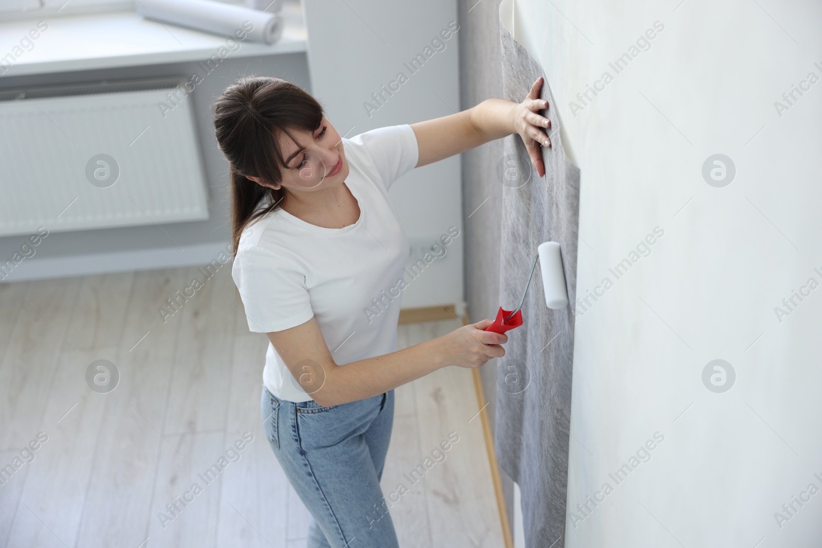 Photo of Woman hanging stylish gray wallpaper in room