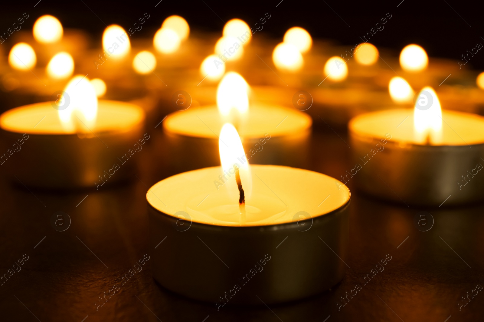 Photo of Burning candles on table in darkness, closeup. Funeral symbol