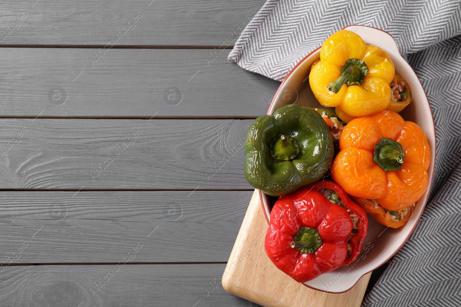 Photo of Tasty stuffed bell peppers in baking dish on grey wooden table, top view. Space for text