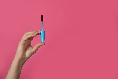 Photo of Woman holding mascara on bright pink, closeup. Space for text