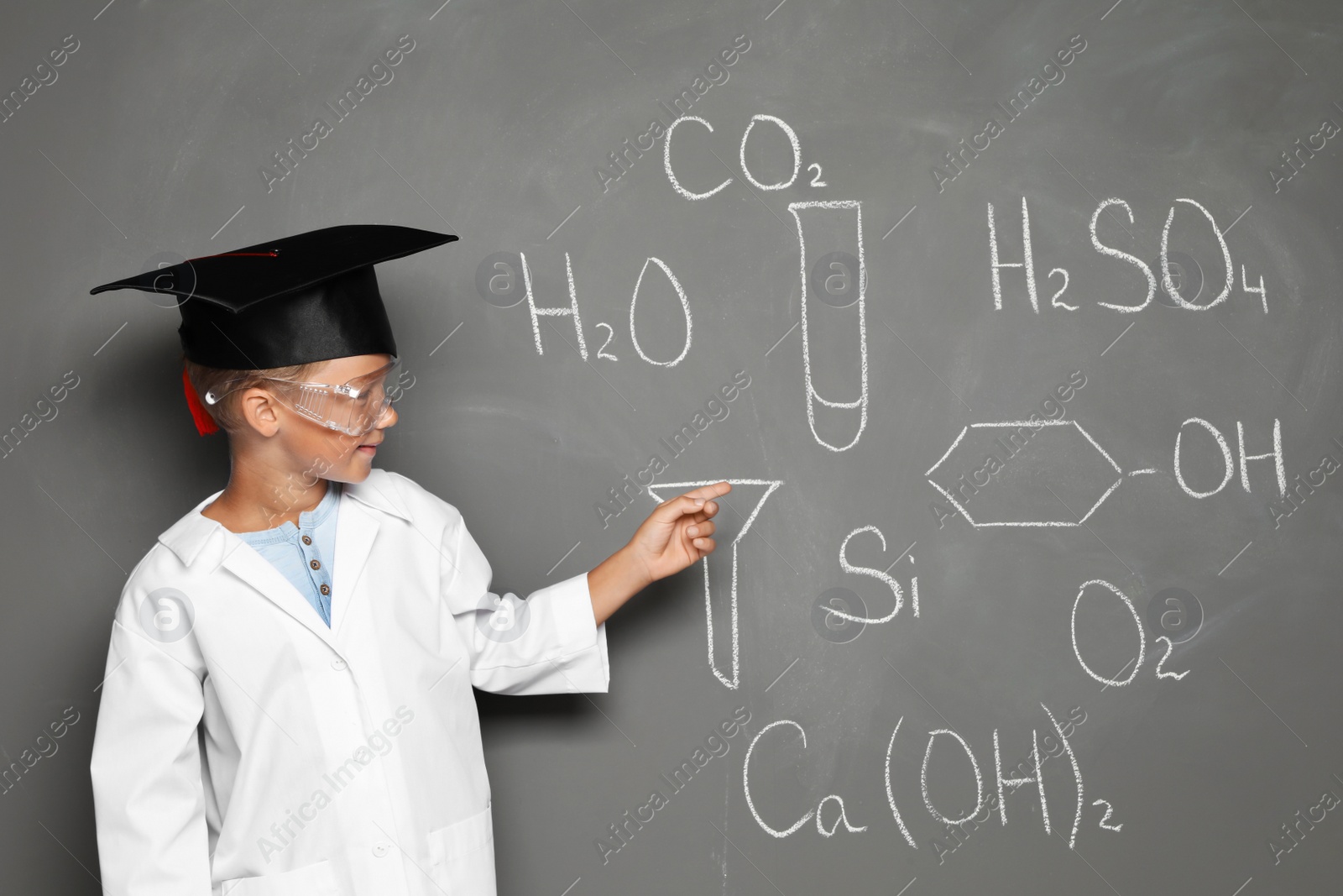 Photo of Little school child in laboratory uniform with graduate cap and chemical formulas on grey background