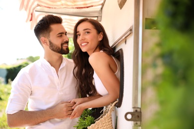 Photo of Happy young woman leaning out of trailer window to hug her boyfriend. Camping vacation