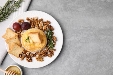 Tasty baked camembert and different products on gray textured table, flat lay. Space for text