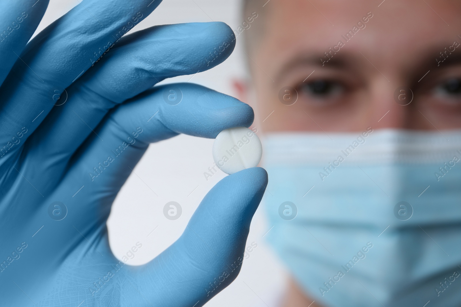 Photo of Doctor holding pill on light background, selective focus