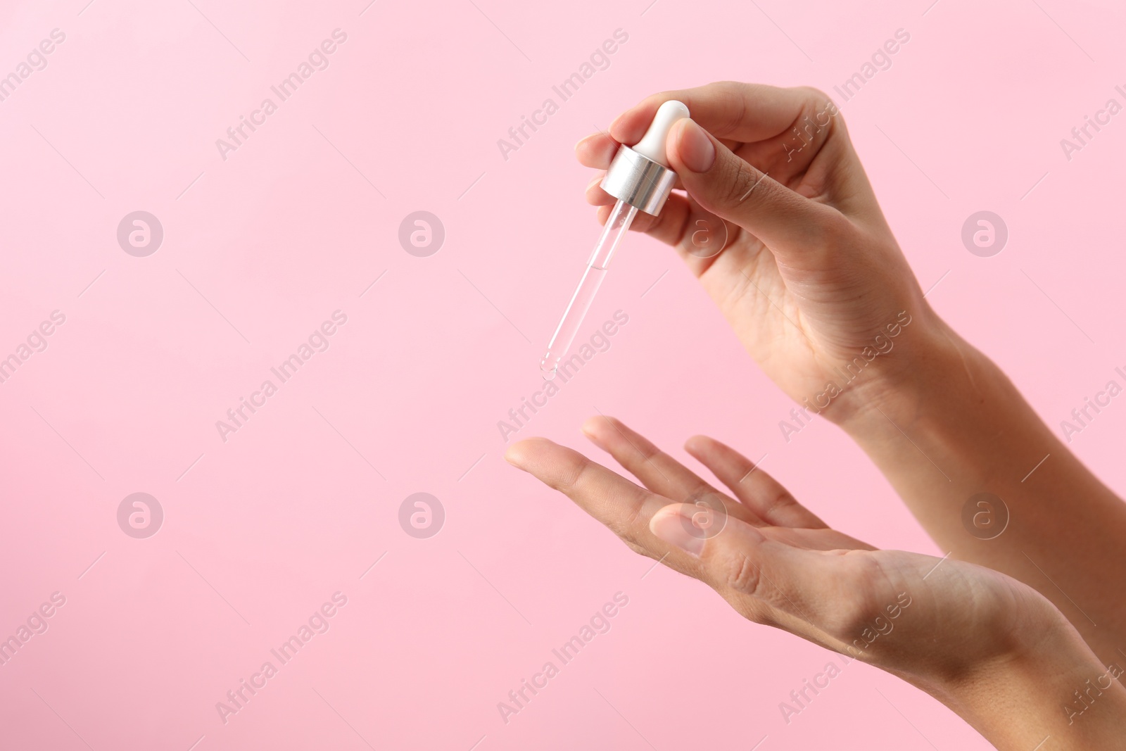 Photo of Woman applying cosmetic serum onto her finger on pink background, closeup. Space for text