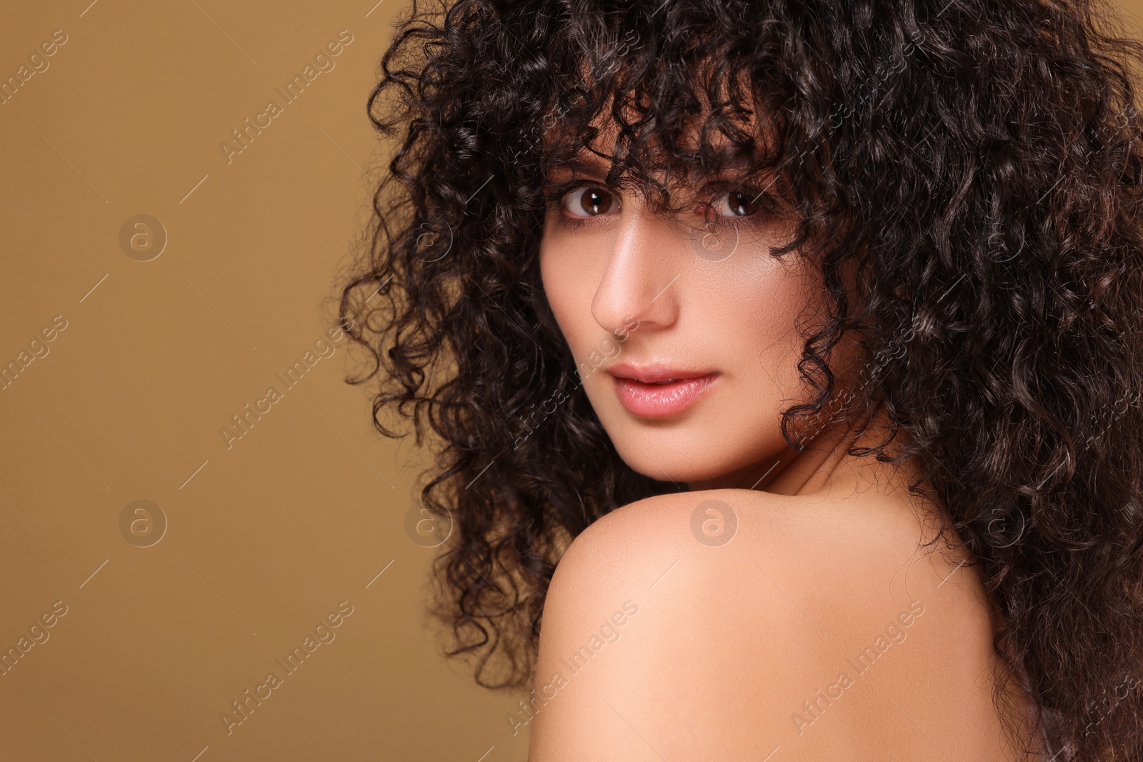 Photo of Beautiful young woman with long curly hair on beige background. Space for text