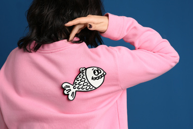 Photo of Woman with paper fish on back against blue background, closeup. April fool's day