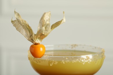 Photo of Refreshing cocktail decorated with physalis fruit on light background, closeup